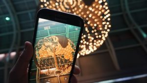 Image is a hand holding phone taking picture of a lighted globe.