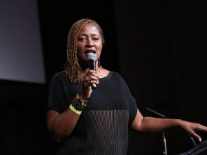 Image is State Senator Holly Mitchell holding a microphone.