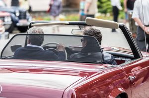 Image is a man and a woman driving a convertible.