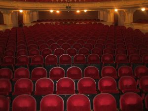 Image is of empty theater seats in an auditorium. Image is of empty theater seats in an auditorium.