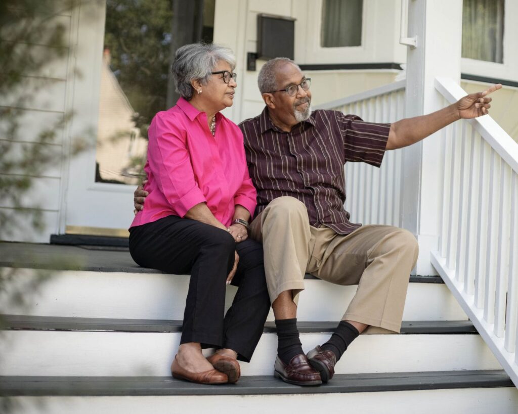 An older couple sit on the front porch of a house remembering the past; letting go of emotional memories is the hardest part of selling a home.