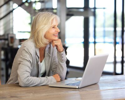 A woman smiles at her laptop knowing that she will stand out while selling her home.