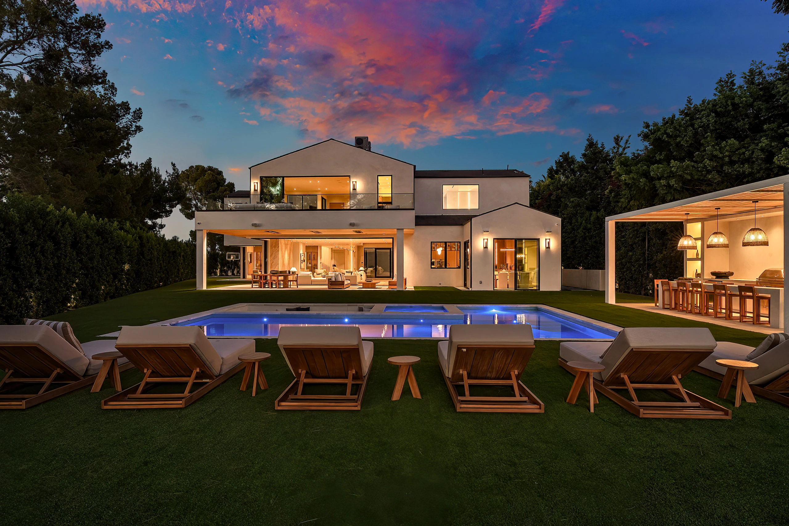 The rear garden, lounge chairs and illuminated pool at dusk