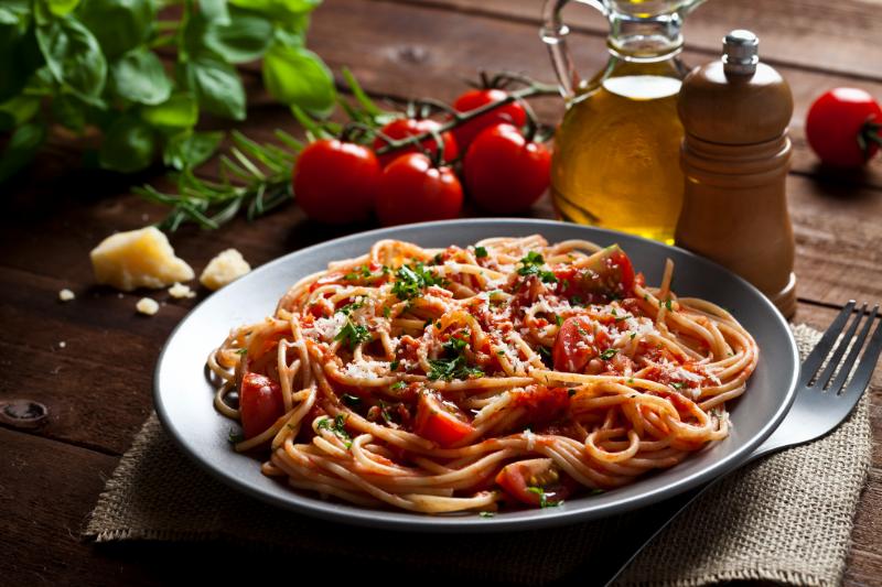 Plate of spaghetti with tomato sauce and herbs on a table with tomatoes and olive oil