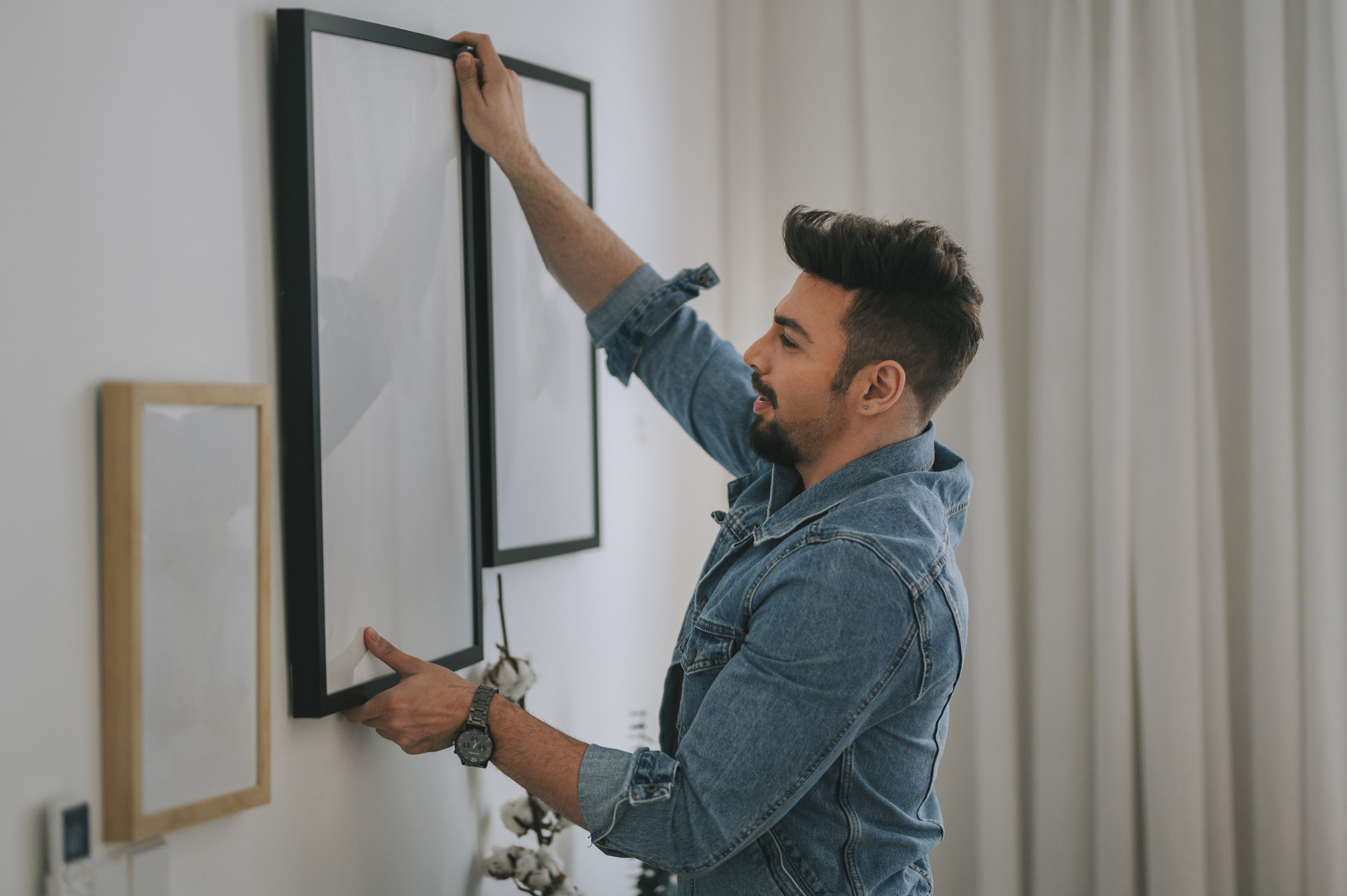 a middle eastern man with beard hanging a painting on the wall at his living room