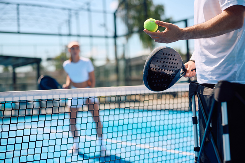 Close up of paddle tennis player serving the ball.