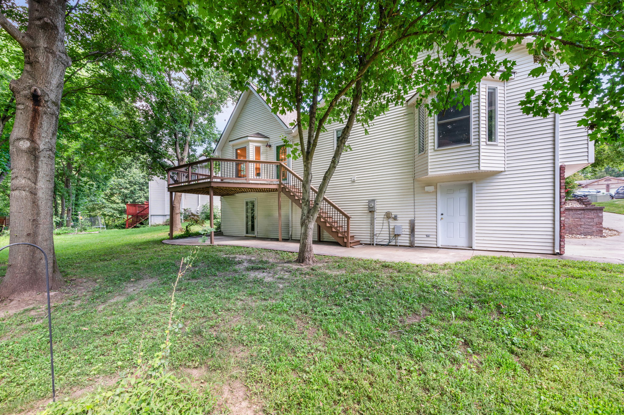 Back of a raised ranch home with a raised deck and walkout lower level under mature trees in Platte City, Missouri