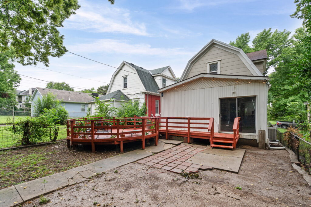 Back of a two-story home with a wraparound wood deck and patio in Kansas City, Missouri