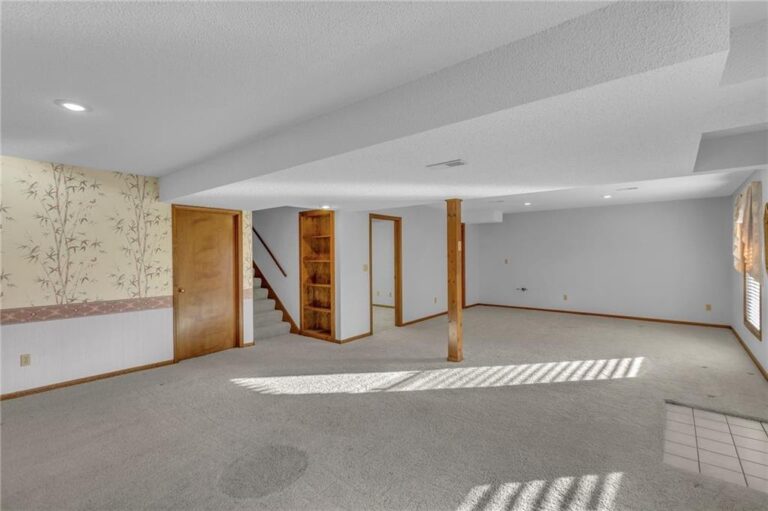Lower-level recreation room with built-in shelving and stairs to the main floor at 7020 N Garfield Avenue in Gladstone, Missouri