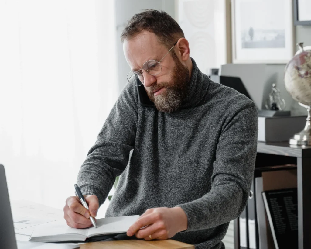 Real Estate Agent at desk taking phone call writing on pad of paper