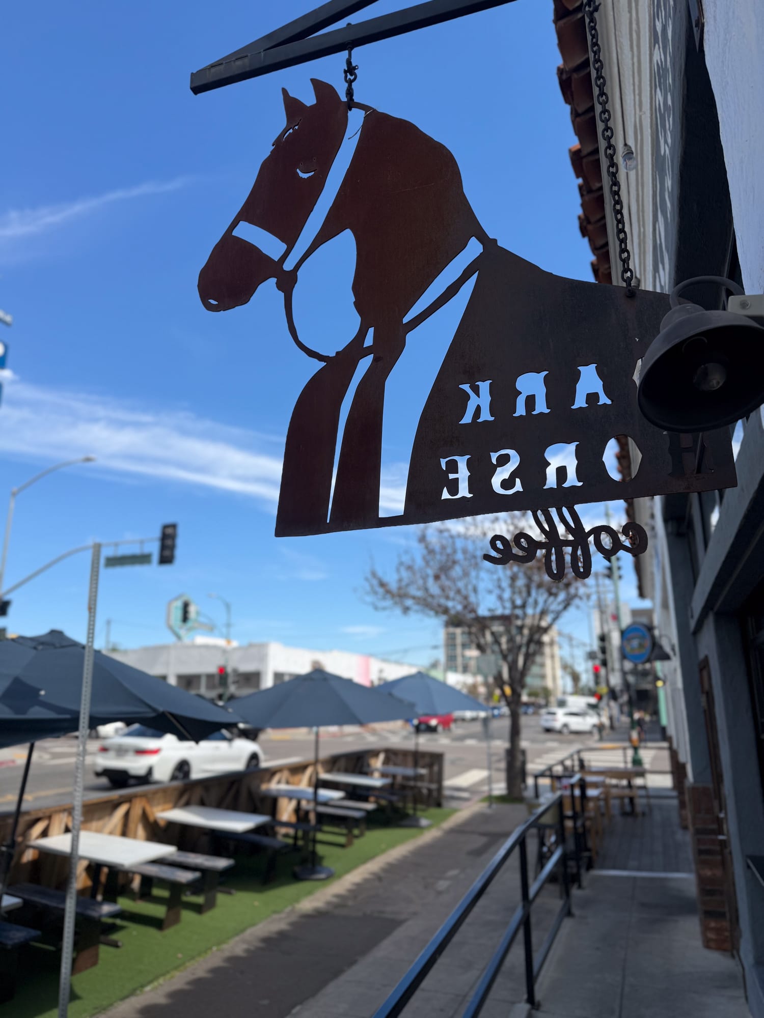Dark Horse Coffee Roasters hanging metal sign with horse logo and outdoor seating on 30th Street North Park