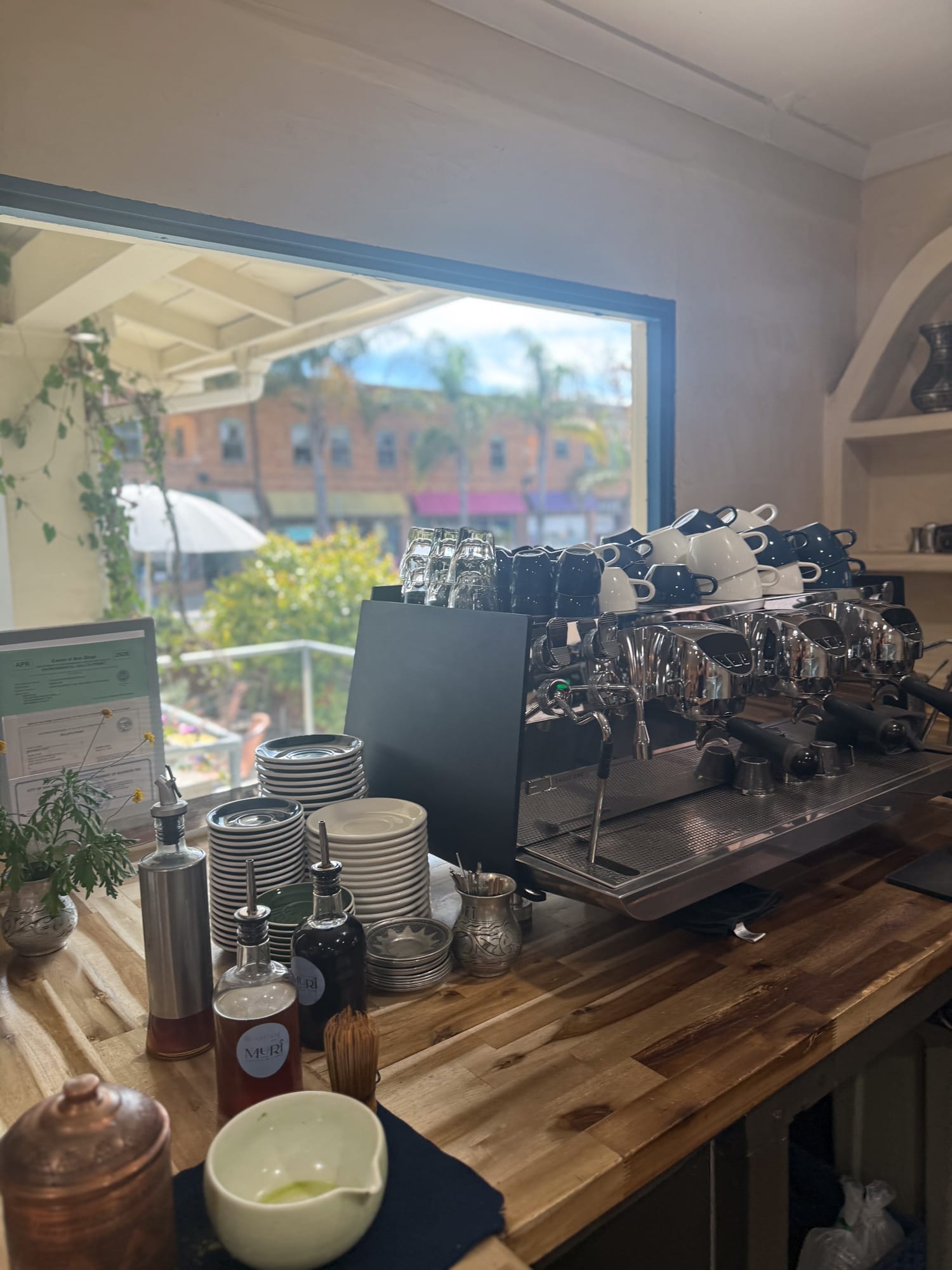 Espresso machine and stacked cups on wood counter inside Muri Coffee in North Park San Diego