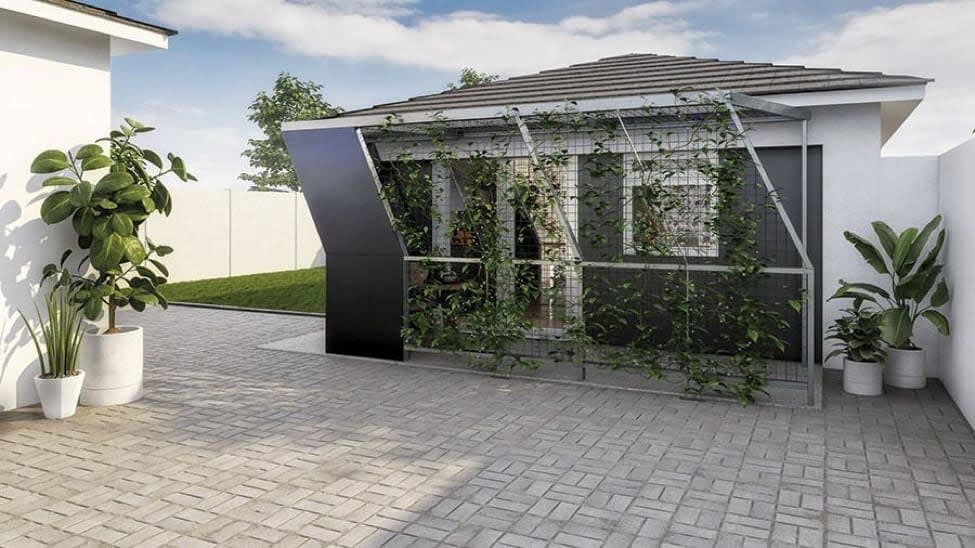 A modern garden shed with a green trellis, surrounded by plants and a paved patio, under a clear sky.