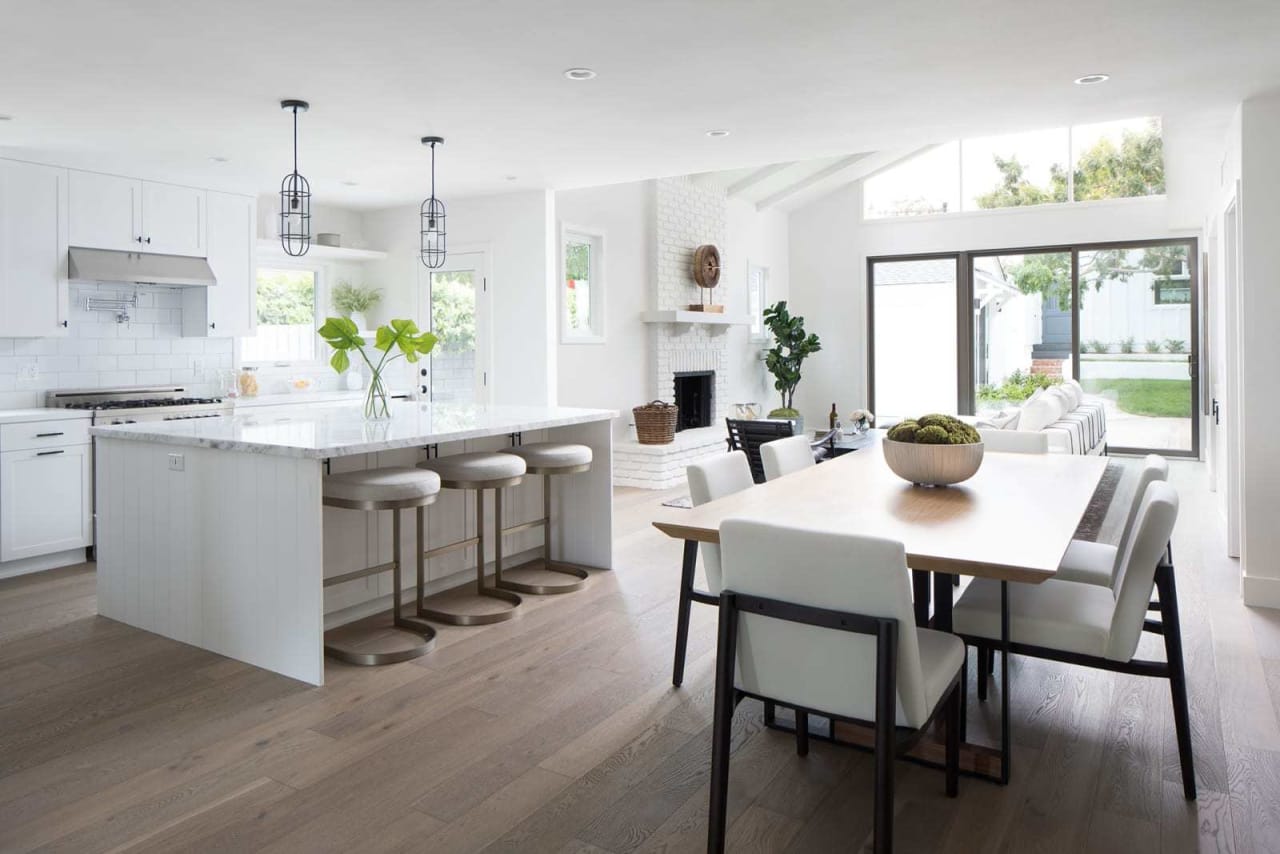 A modern kitchen and dining area with white cabinetry, a large island, and a dining table. Bright, airy space with natural light.