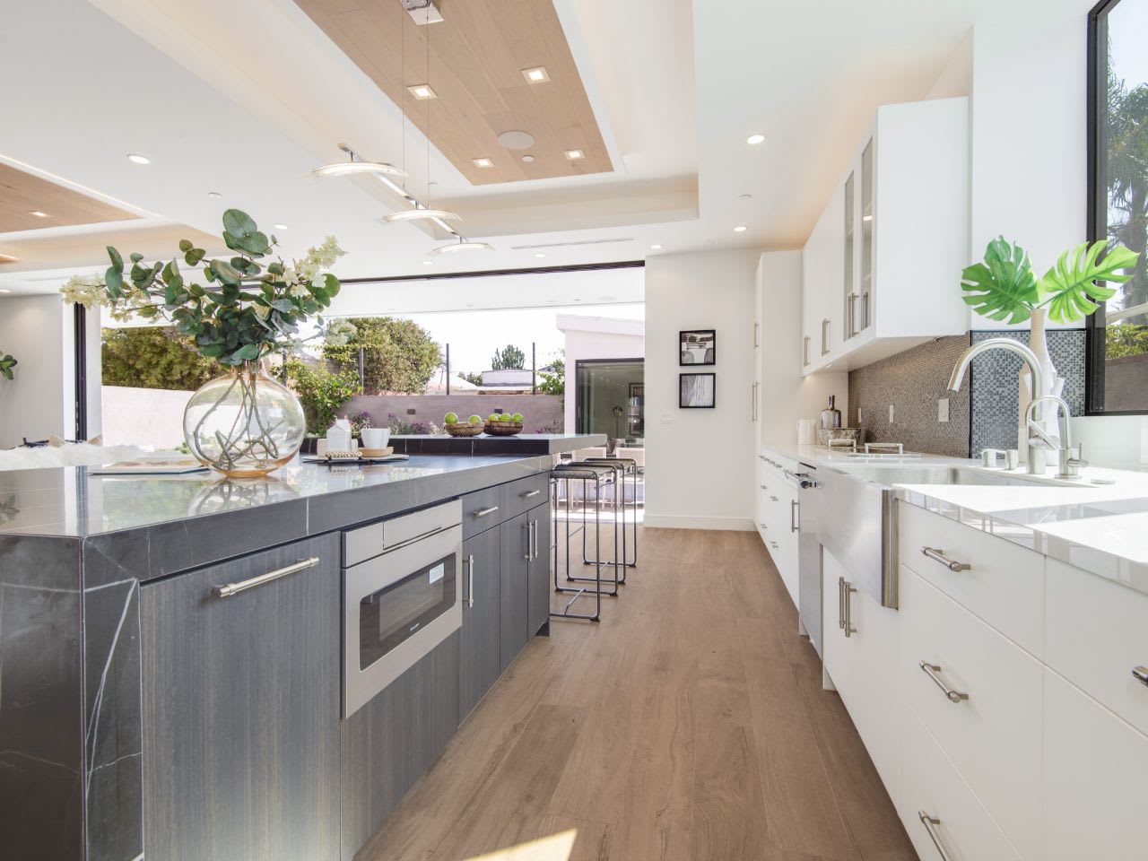 Modern kitchen with a large island, sleek cabinetry, and natural light. Features plants and stylish decor.