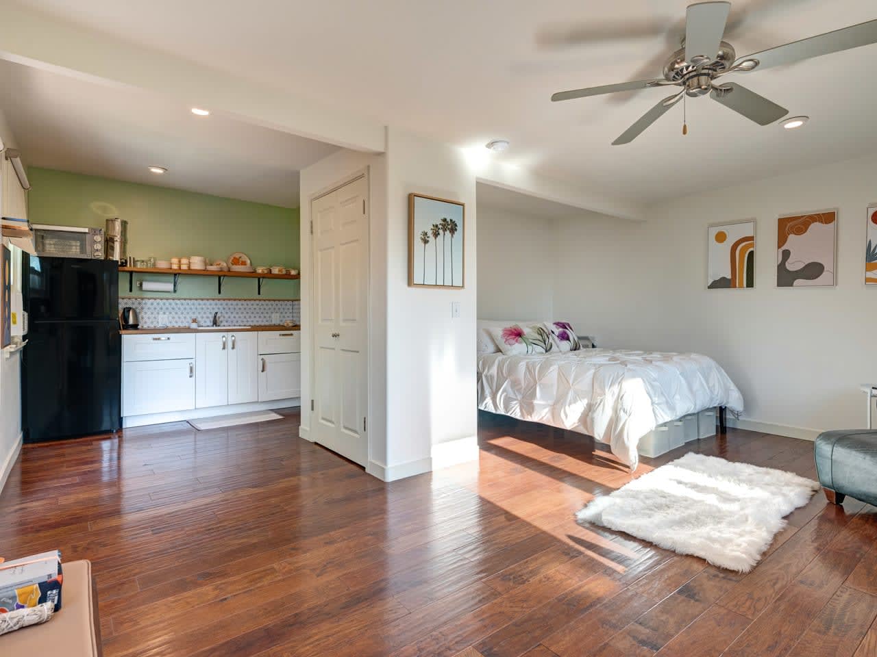A cozy studio with a kitchen area, a bed with floral pillows, wooden floors, and modern decor.