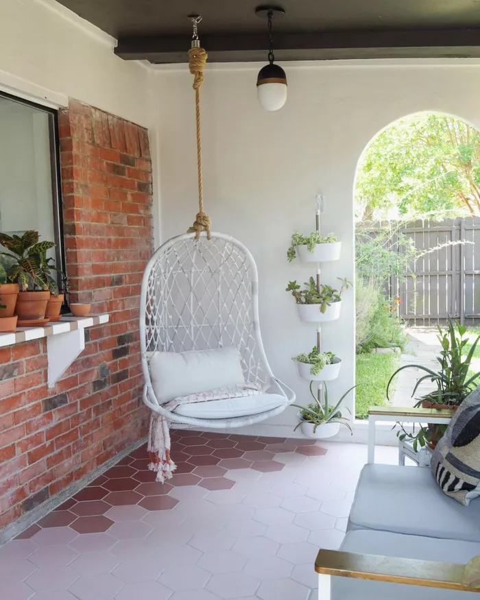 A swing chair hanging in the corner of an outdoor room.