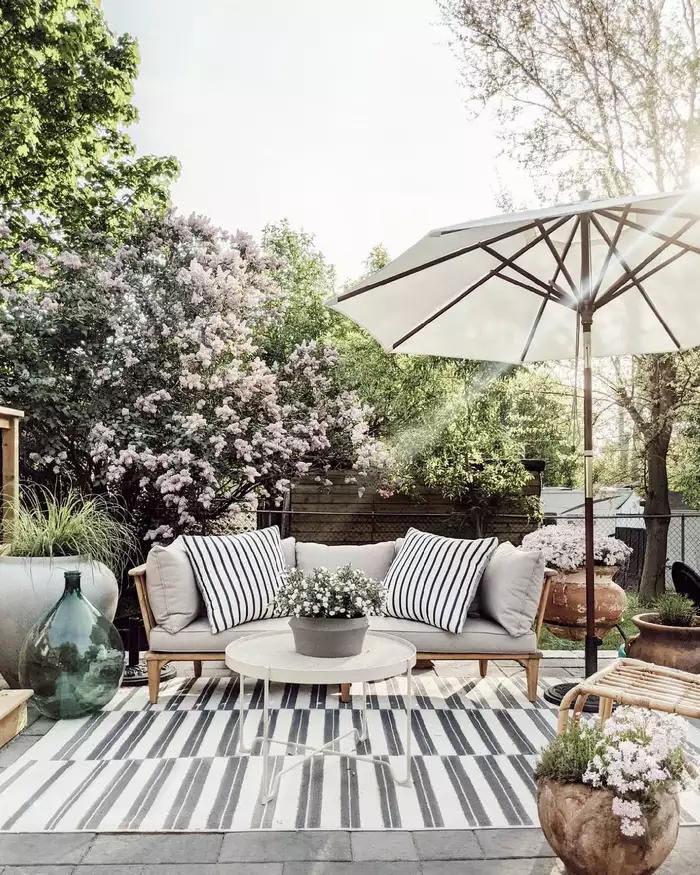A spring inspired outdoor living room with an umbrella, love seat and rug.