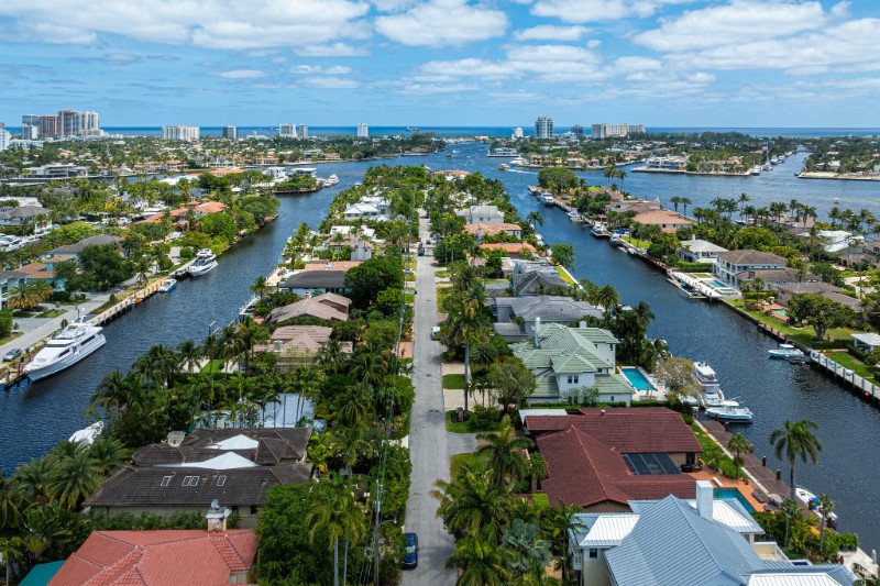 Aerial view of Rio Vista, Fort Lauderdale, highlighting a residential neighborhood with tree-lined streets, luxury homes, and canals weaving through the community, with the downtown skyline and Atlantic Ocean visible in the background.