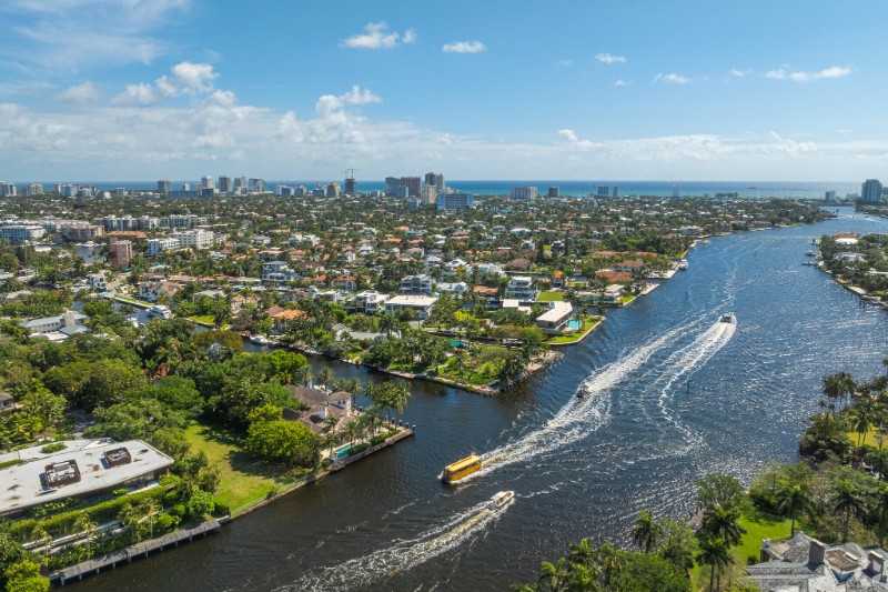 Aerial view of Las Olas Isles in Fort Lauderdale, showcasing upscale waterfront homes lined along narrow islands with private docks and yachts, surrounded by an intricate network of canals leading to the Intracoastal Waterway and ocean.