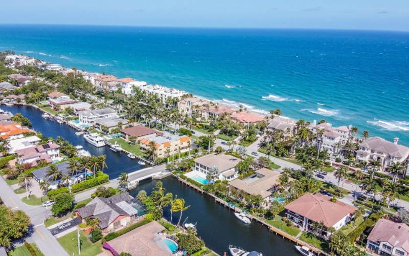Aerial view of Highland Beach, Florida, showing a narrow strip of luxury waterfront homes nestled between the Atlantic Ocean and the Intracoastal Waterway, with turquoise waves rolling onto the sandy shoreline and boats docked behind many properties.