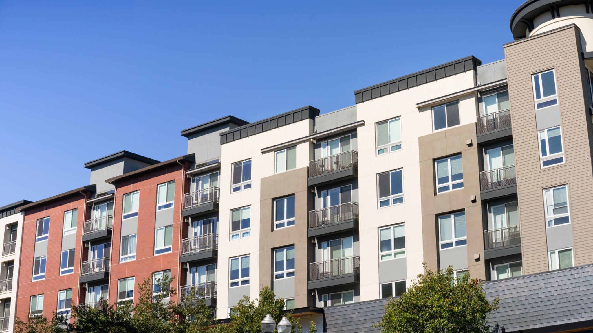 Modern multi-story apartment building exterior with balconies under a clear blue sky.