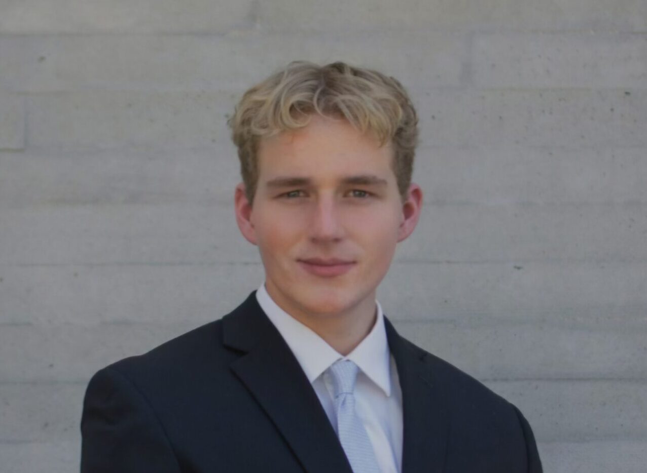 James "Jase" Joseph with arms crossed in front of a white brick building and tree, during a property inspection.