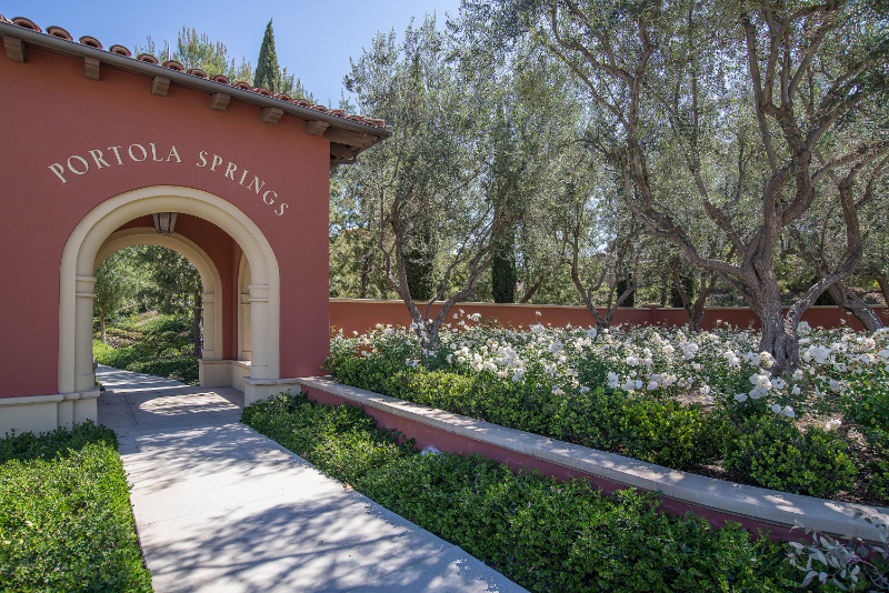 Portola Springs village entry archway in Irvine, framed by olive trees and a landscaped walking path.