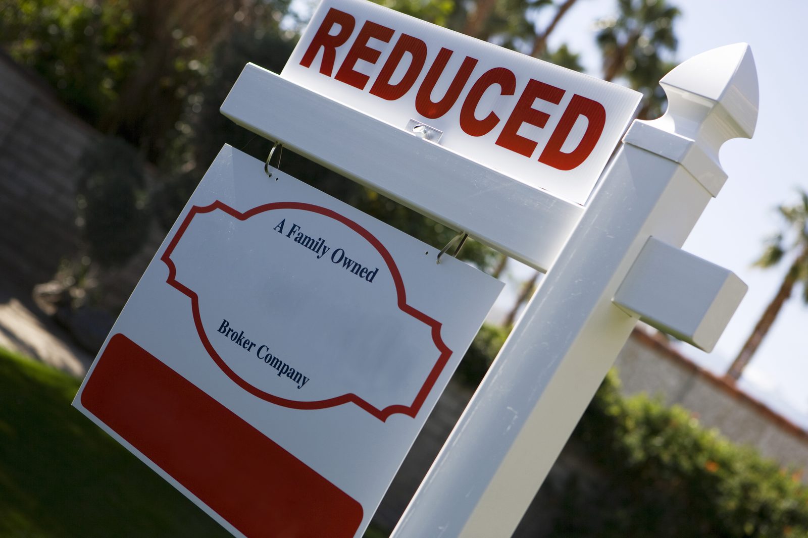 A red "Reduced" rider on a real estate for sale sign in front of a home