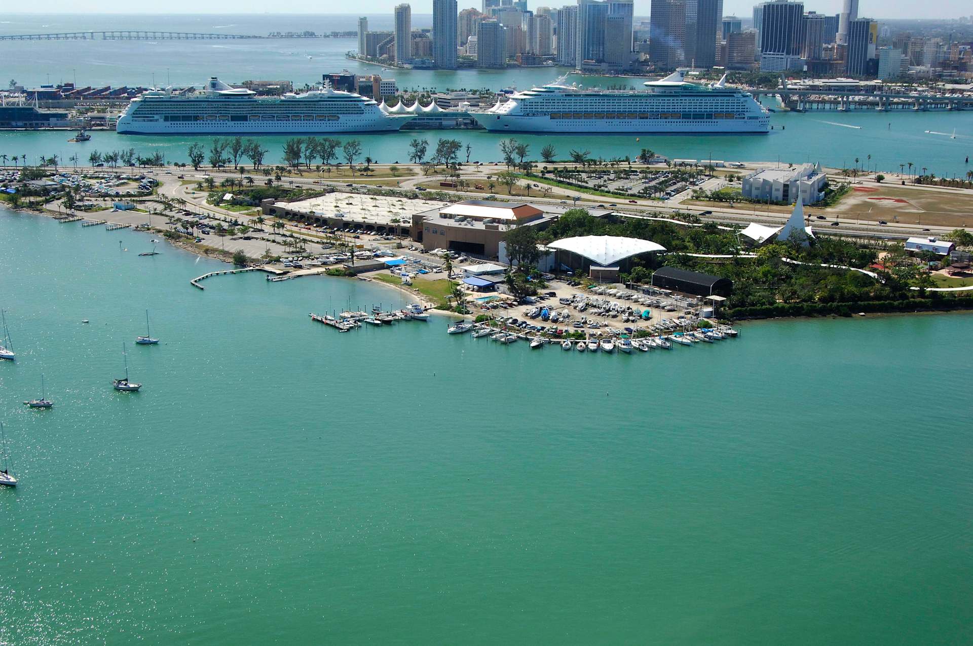 Aerial view of a marina with boats, surrounded by water and city skyline in the background.