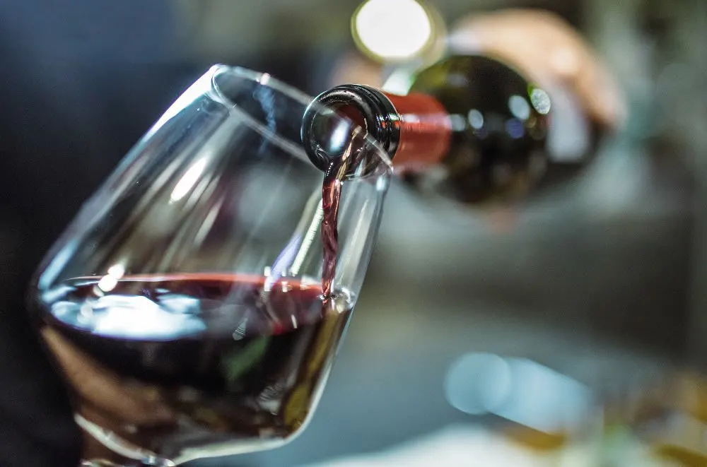A close-up of a red wine bottle pouring into a glass, capturing the rich color and fluid motion.