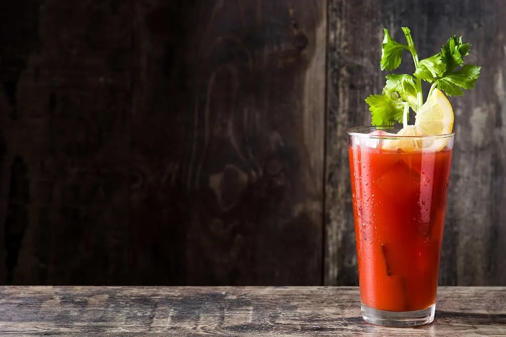 A tall glass of red cocktail garnished with lemon and cilantro, set against a dark wooden background.