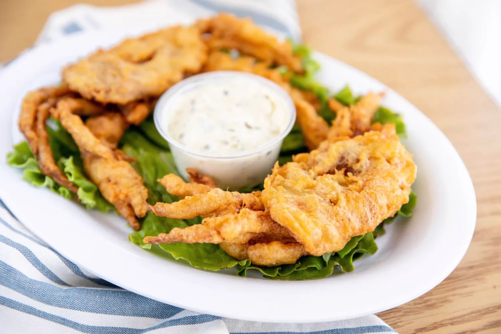 A plate of fried food, including crispy pieces on lettuce, accompanied by a small cup of dipping sauce.
