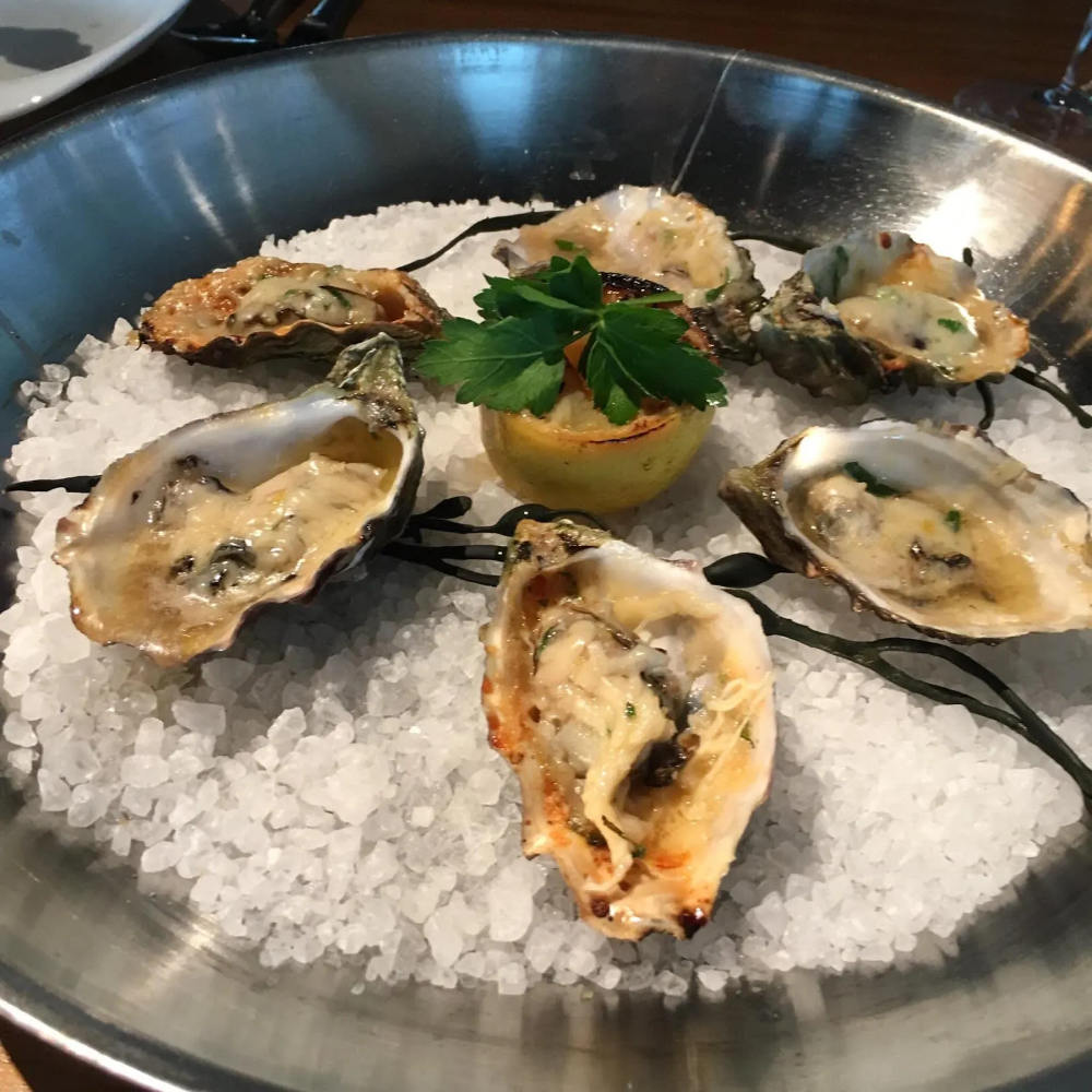 A platter of baked oysters on a bed of ice, garnished with a grilled lemon and parsley.