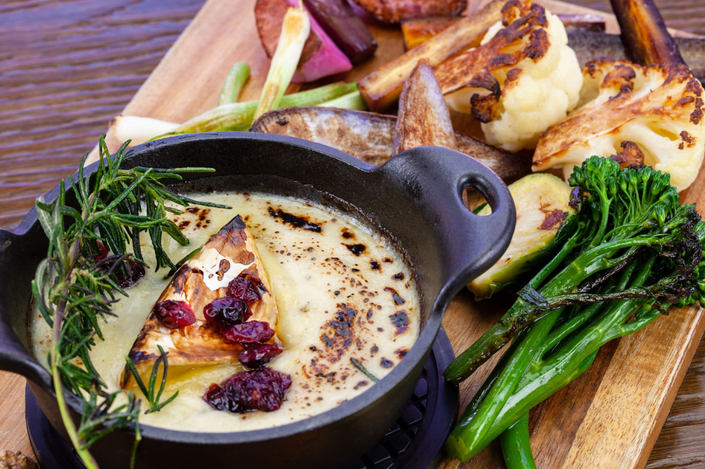 A cast iron pot with creamy dish topped with herbs and cranberries, alongside roasted vegetables on a wooden board.
