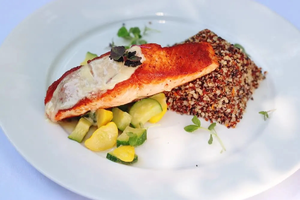 A plate featuring grilled salmon, quinoa, and sautéed zucchini and squash, garnished with fresh herbs.