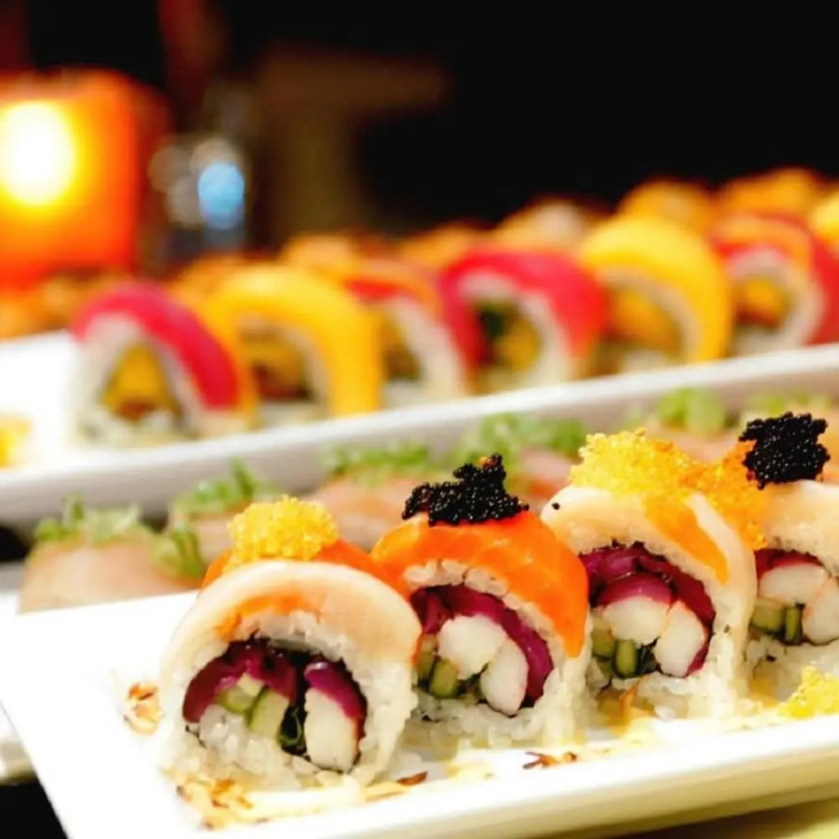 A colorful assortment of sushi rolls on a white plate, featuring various toppings and garnishes.
