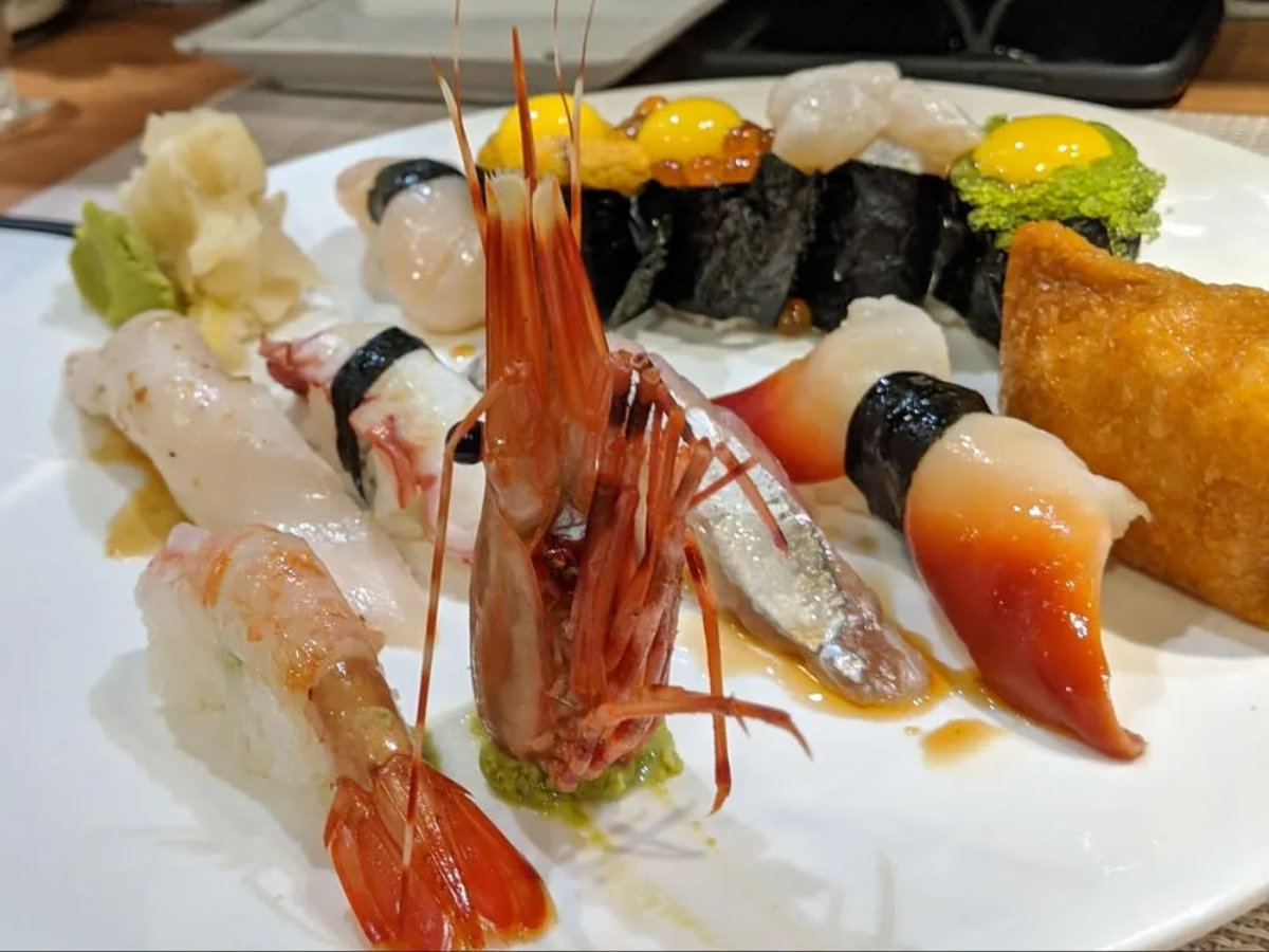 A plate of assorted sushi, featuring shrimp, fish, and seaweed rolls, garnished with wasabi and pickled ginger.