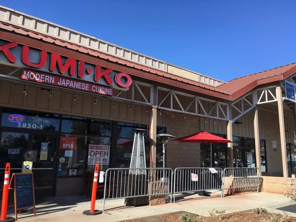 Exterior of Kumi-Ko restaurant featuring a red umbrella, open sign, and modern Japanese cuisine branding.