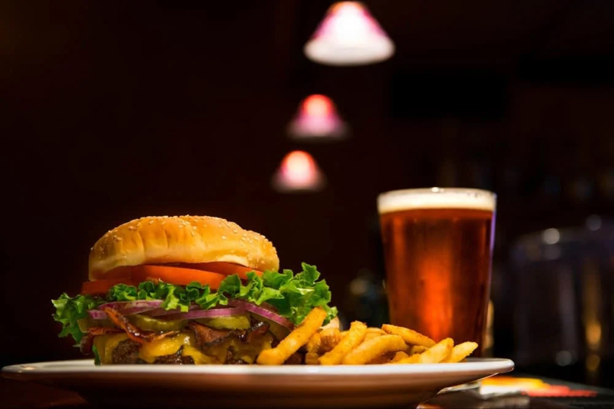 A delicious cheeseburger with lettuce, tomato, and onion, served with fries and a glass of beer in a dimly lit setting.