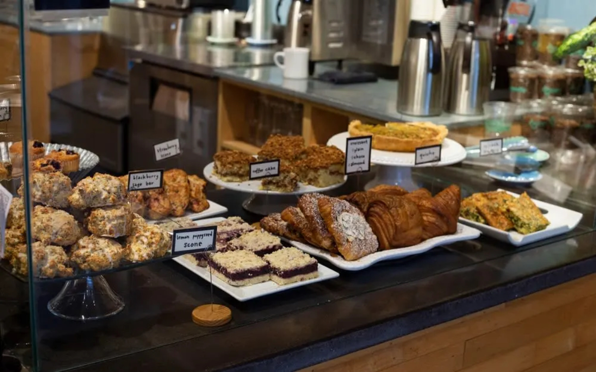 A display of various baked goods, including scones, coffee cake, croissants, and bars, in a café setting.