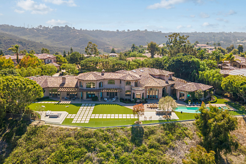 Aerial view of a sprawling Mediterranean-style luxury estate with terracotta roof tiles, extensive landscaped grounds, a large pool, outdoor seating areas, and scenic views of surrounding hills and greenery.