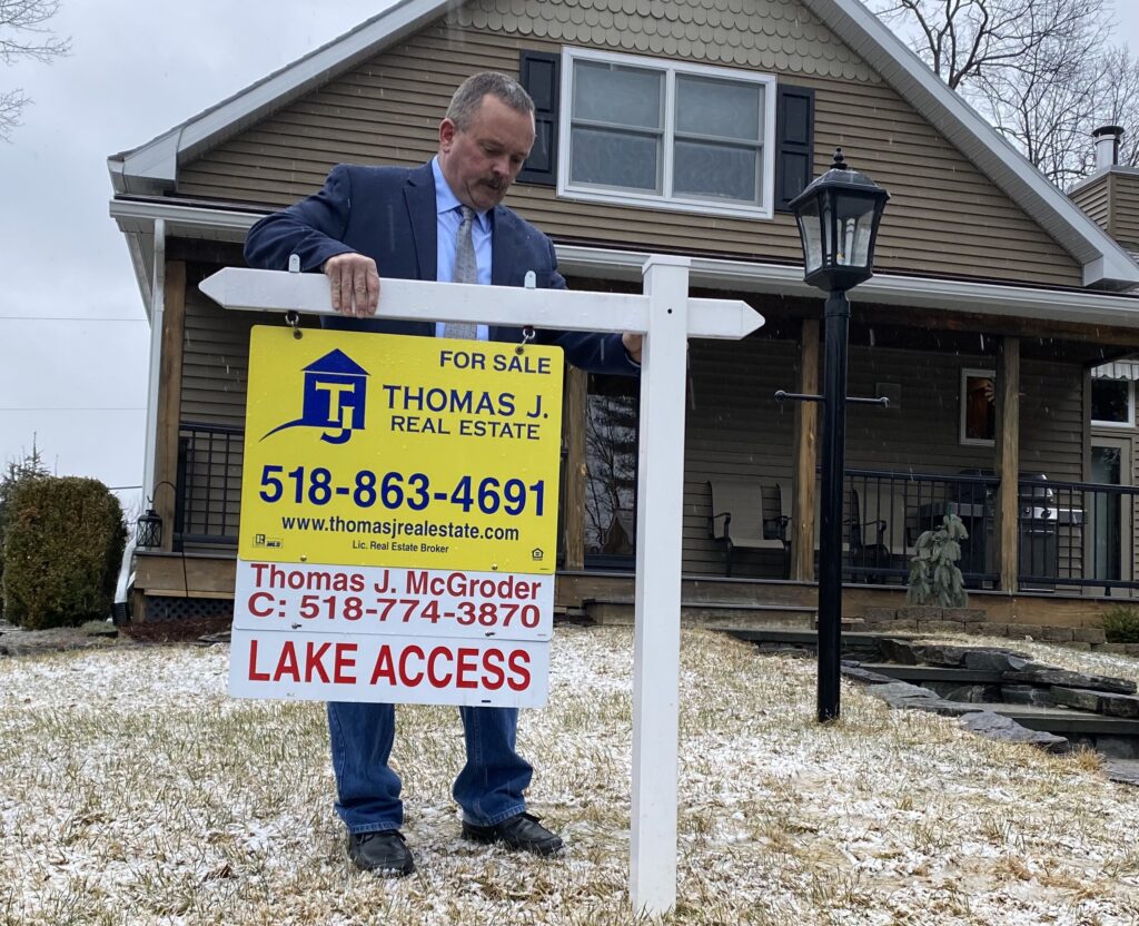 Real estate agent installing a for sale sign at a home in upstate New York for a home value estimate NY blog