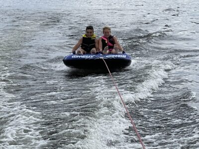 Two people riding a towable tube behind a boat on the Great Sacandaga Lake, enjoying calm water and summer boating conditions.