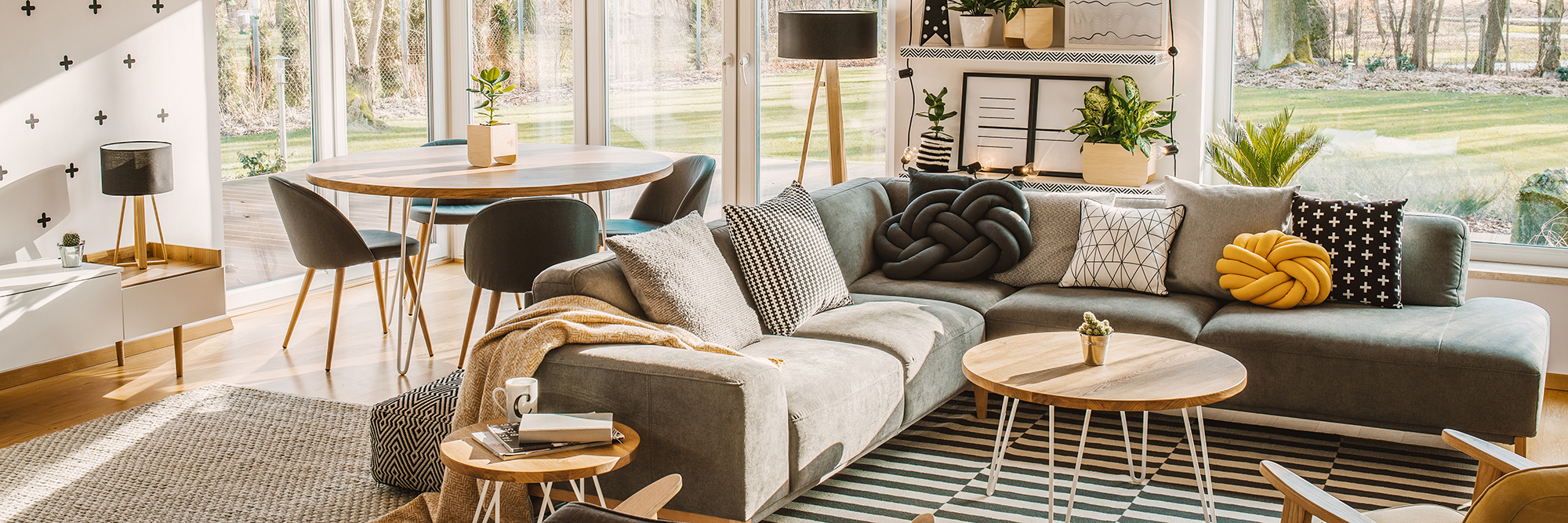 Side angle of a corner sofa with pillows and dining table with chairs behind in a bright living room interior