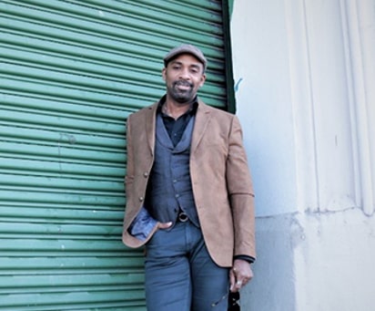 bearded man in a brown coat, undershirt and jeans