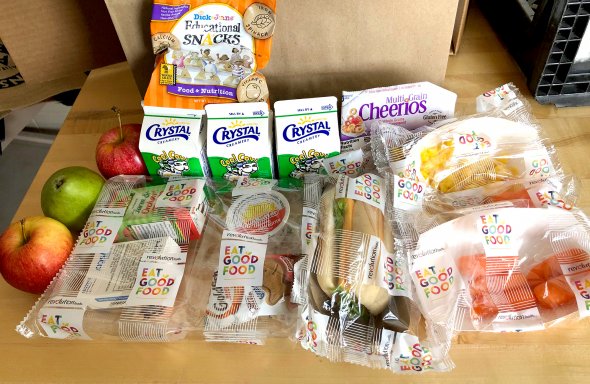Image of Grab & Go Meals offered at John Muir Elementary, including wrapped sandwiches, boxed milk, apples, carrots, and packaged snacks