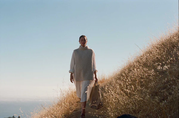 Image of Woman Walking Through Field wearing Neutral Bohemian Chic Outfit and holding Purse from Reliquary SF