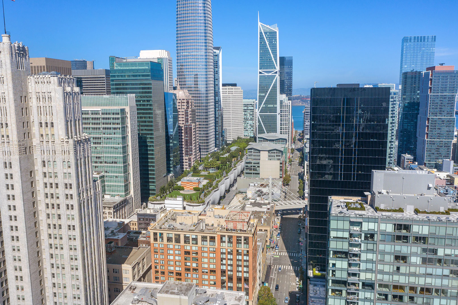 Aerial view looking down on the lush green lawns and winding paths of Yerba Buena Gardens, surrounded by sleek glass and steel highrise buildings.