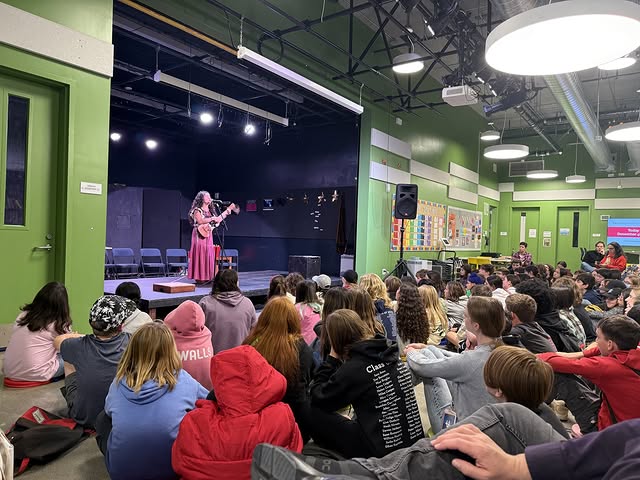 Students in audience at school auditorium watching a classmate play the guitar and sing at a talent show